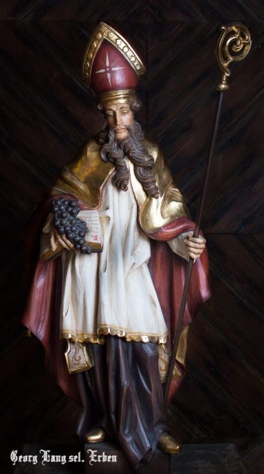 Figur eines Heiligen in traditioneller Kleidung mit Stab und Buch.