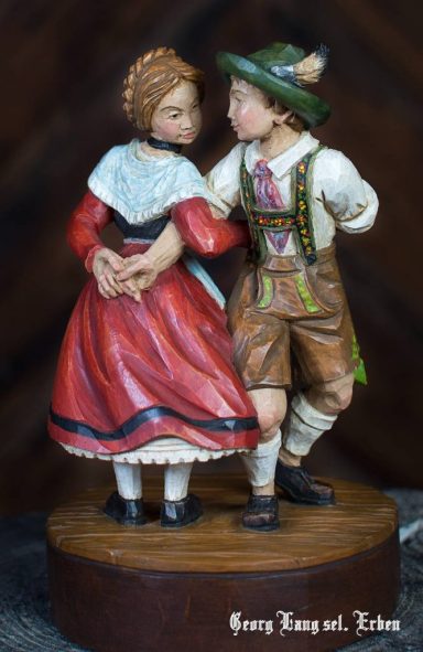 Ein Paar in traditionellen Trachten tanzt, männlich und weiblich, auf einem Sockel.