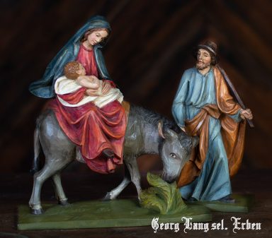 Maria mit dem Jesuskind auf einer Eselin, Josef steht daneben in traditioneller Kleidung.