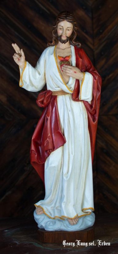 Statue von Jesus Christus, mit erhobenem Finger und rotem Gewand, steht auf einem Sockel.