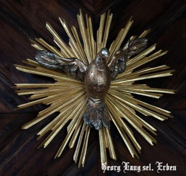 Goldener, strahlender Heiliggeist mit erhobenen Flügeln, umgeben von goldenen Strahlen.
