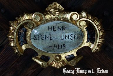 Schmuckelement mit der Inschrift "Herr, segne unser Haus" in goldener Schrift.